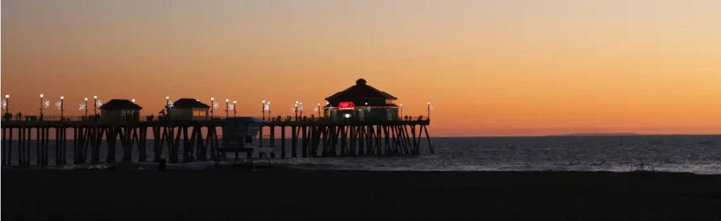 Silhouetted view of Huntington Beach pier at sunset, with a glowing sky and calm ocean, highlighting a popular area for jumbo mortgages in California.