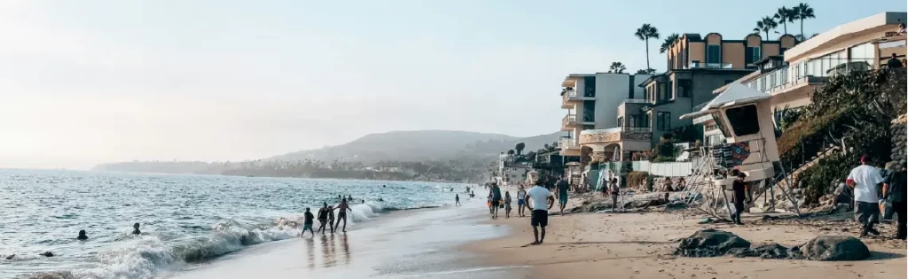 People enjoying a sunny day on the beach in Laguna Beach, California, with luxury homes along the shore, a prime area for jumbo mortgages.