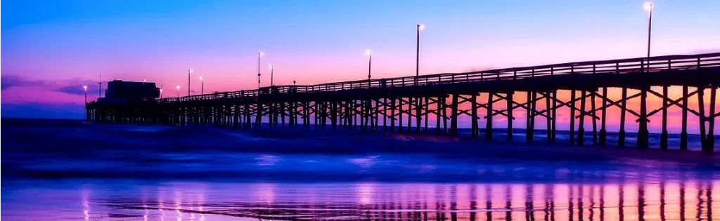 Newport Beach pier at sunset with vibrant purple and pink skies reflecting on the water, showcasing a coastal area for jumbo mortgages in California.