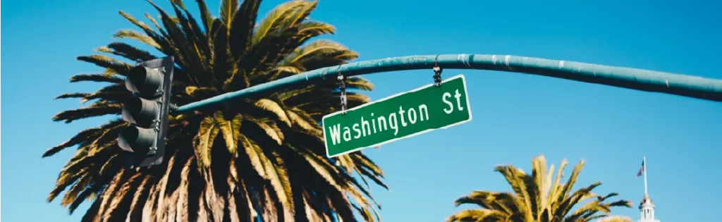 Street sign reading “Washington St” against a clear blue sky with a palm tree in the background.