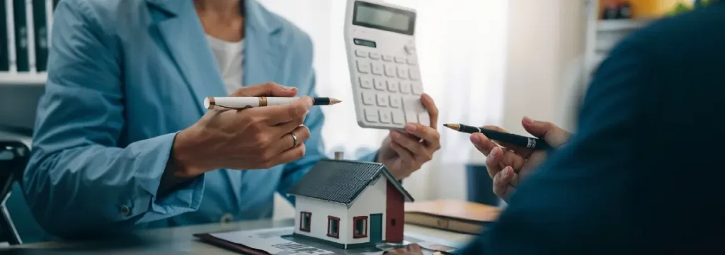 Two people discussing mortgage details with a model house and calculator, representing home loan planning.