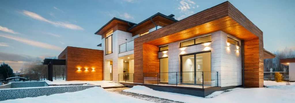 Modern wooden house illuminated at dusk, showcasing sleek design against a snowy landscape.